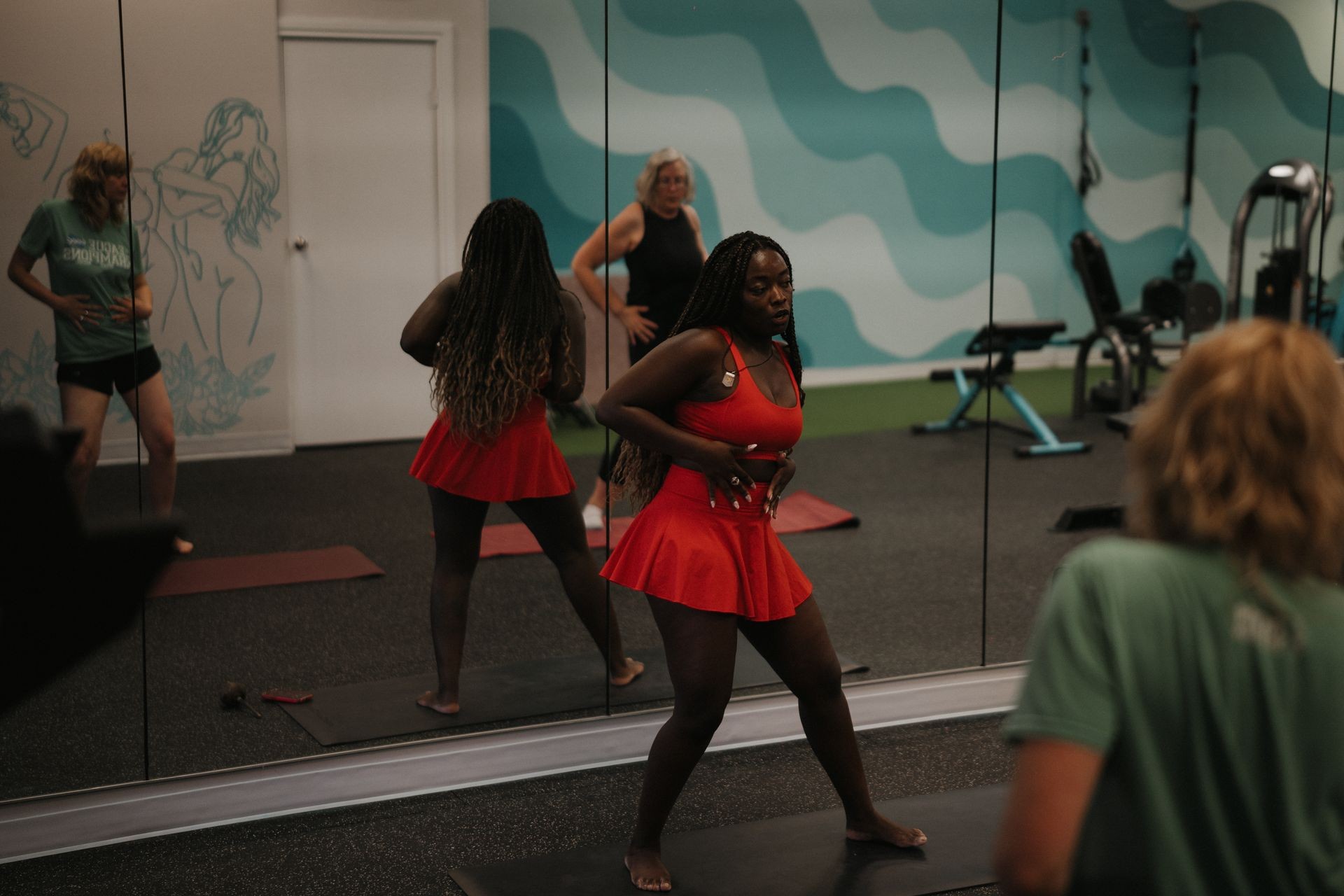 Individuals in workout attire performing exercises in front of a large mirror in a brightly colored fitness room.